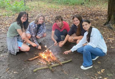 Gruppo di adolescenti che arrostiscono i marshmallow attorno al fuoco nei campi estivi in Inghilterra
