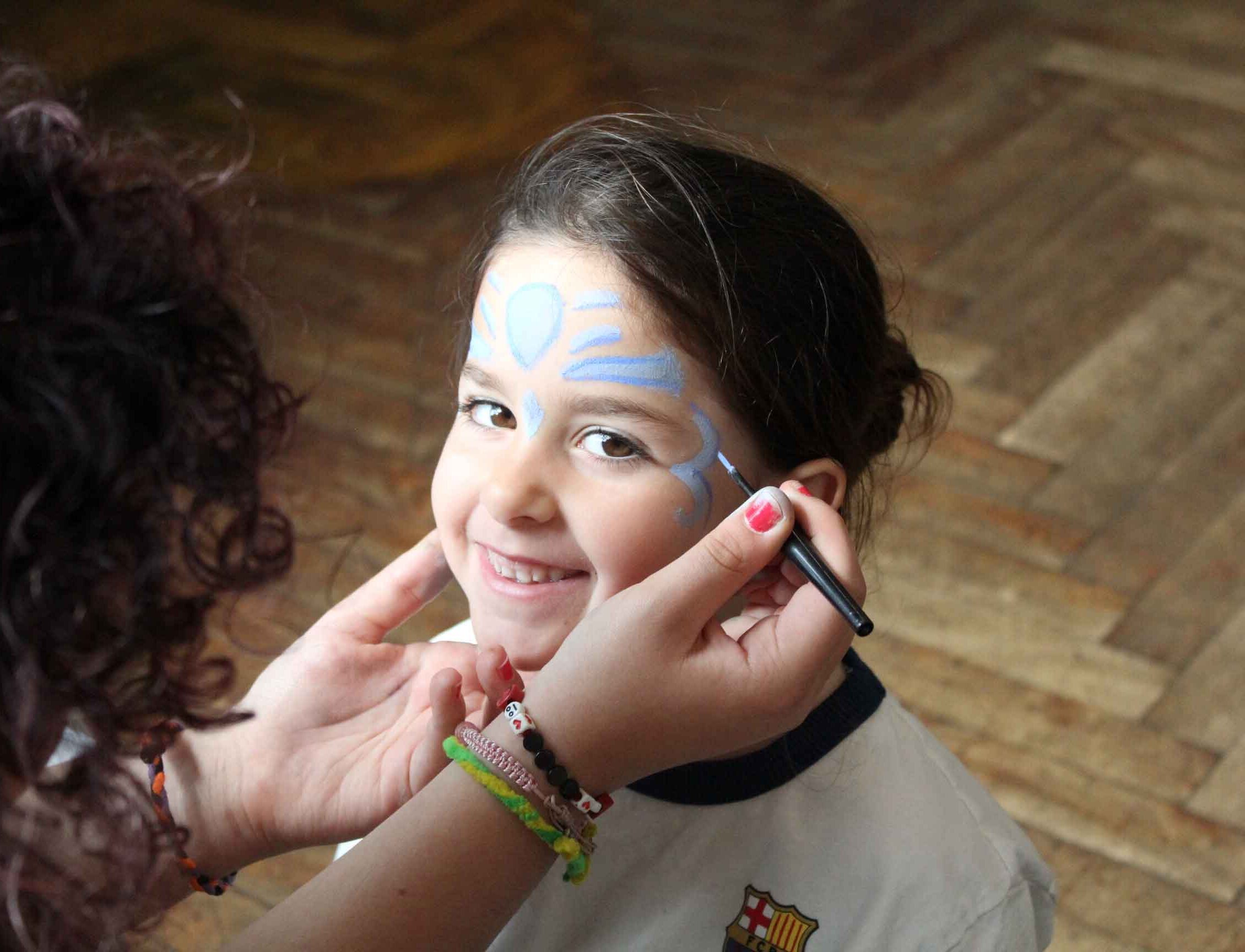 Girl smiles as she has her face painted by staff member at XUK Day camp