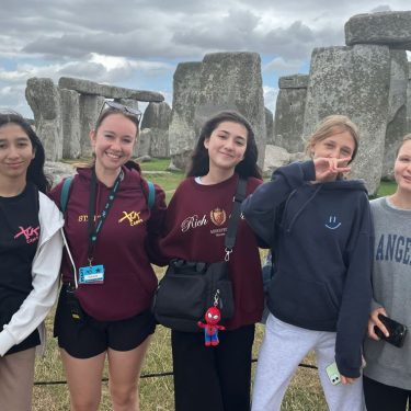 Counselor guiding a group of smiling campers on a trip to stoneheng and promoting summer camp counselor jobs for 2026 at XUK Camps